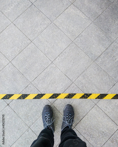 Top view of a man stands on industrial striped asphalt floor in front warning yellow black pattern and stop sign.