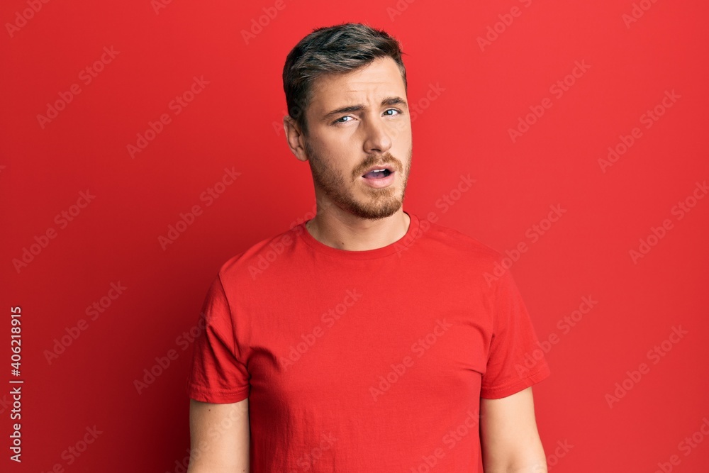 Handsome caucasian man wearing casual red tshirt in shock face, looking skeptical and sarcastic, surprised with open mouth Handsome caucasian man wearing casual red tshirt in shock face, looking skeptical and sarcastic, surprised with open mouth