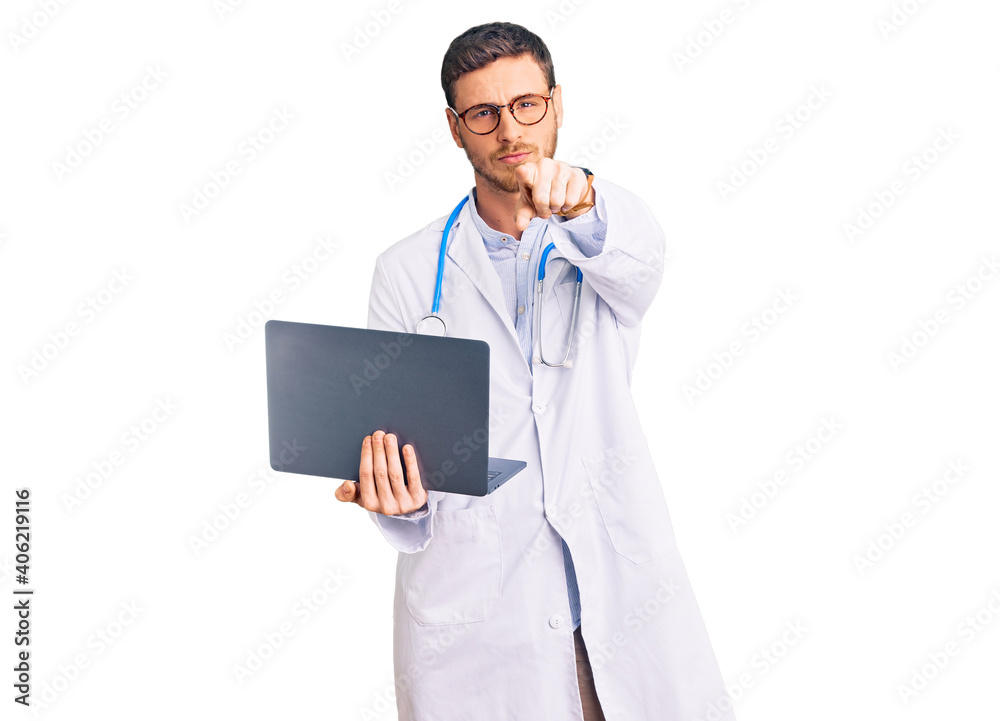 Handsome young man with bear wearing doctor uniform working using computer laptop pointing with finger to the camera and to you, confident gesture looking serious Handsome young man with bear wearing doctor uniform working using computer laptop pointing with finger to the camera and to you, confident gesture looking serious