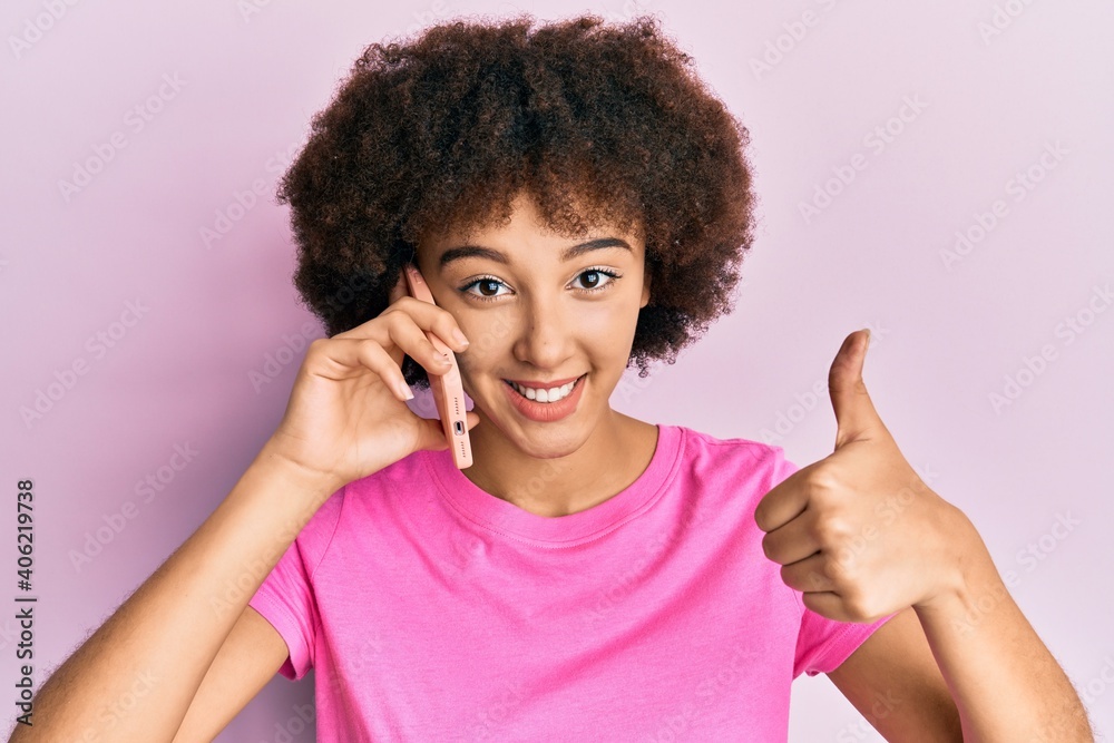 Young hispanic girl having conversation talking on the smartphone smiling happy and positive, thumb up doing excellent and approval sign Young hispanic girl having conversation talking on the smartphone smiling happy and positive, thumb up doing excellent and approval sign