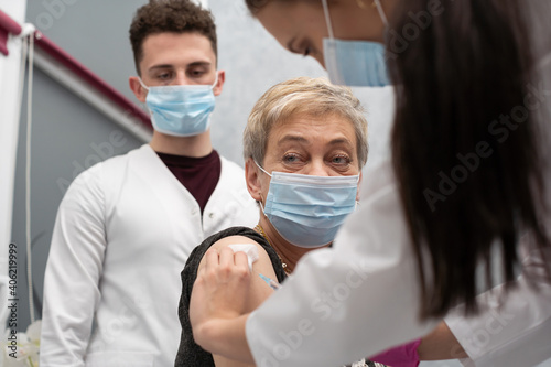 A nurse is making an vaccine to an elderly woman. The COVID vaccine19. A sterile doctor's office in a private clinic. A young medical intern looks at how to properly inject.
