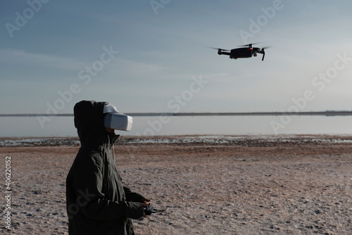 Tourist exploring new places. Drone pilot on nature with quadcopter. Using drone while standing near lake. Young person  with drone and virtual reality viewer.