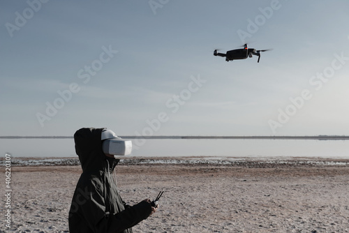 Tourist exploring new places. Drone pilot on nature with quadcopter. Using drone while standing near lake. Young person with drone and virtual reality viewer.