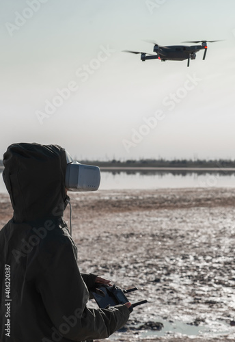 Tourist exploring new places. Drone pilot on nature with quadcopter. Using drone while standing near lake. Young person  with drone and virtual reality viewer.