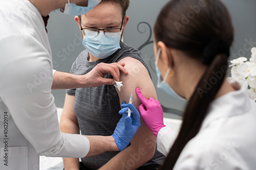 A young intern learns to inject a COVID19 vaccine into a young adult patient. A sterile doctor s office in a private clinic. A young nurse teaches a medical intern how to properly inject.