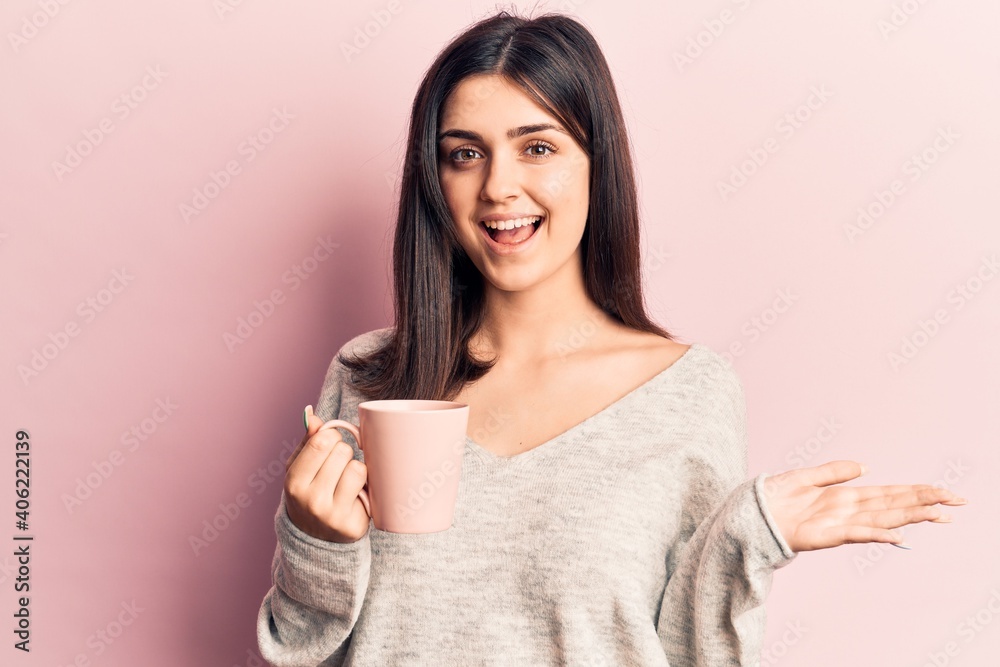 Young beautiful girl drinking mug of coffee celebrating achievement with happy smile and winner expression with raised hand Young beautiful girl drinking mug of coffee celebrating achievement with happy smile and winner expression with raised hand