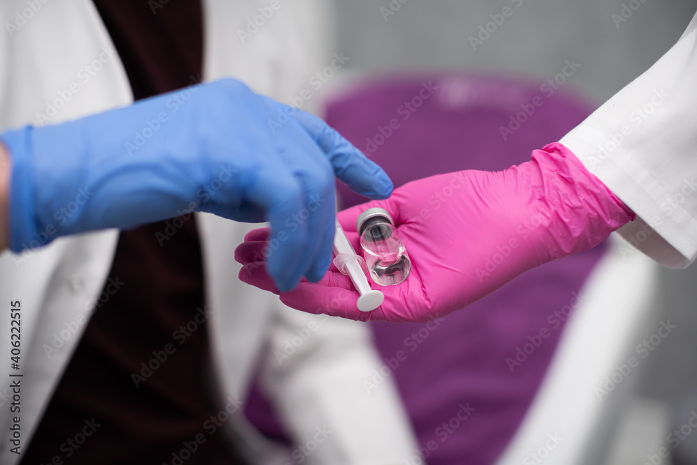 The doctor gives the trainee a vial with a medicine and a syringe as a set for injections, including flu and COVID19 vaccines. A sterile doctor's office in a private clinic. The doctor gives the trainee a vial with a medicine and a syringe as a set for injections, including flu and COVID19 vaccines. A sterile doctor's office in a private clinic.