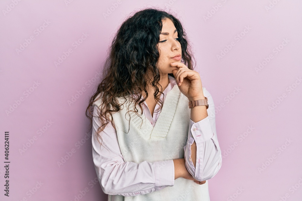 Young brunette woman with curly hair wearing casual clothes with hand on chin thinking about question, pensive expression. smiling with thoughtful face. doubt concept. Young brunette woman with curly hair wearing casual clothes with hand on chin thinking about question, pensive expression. smiling with thoughtful face. doubt concept.