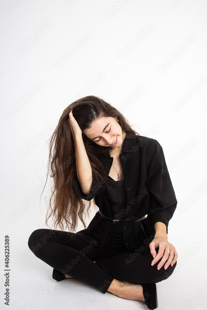 Attractive young woman with long brown hair in black clothes sitting on white background. Vertical view Attractive young woman with long brown hair in black clothes sitting on white background. Vertical view