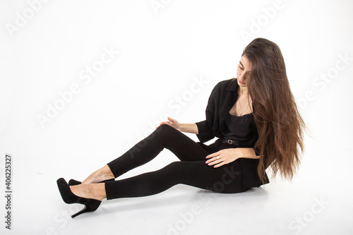 Attractive young woman with long brown hair in black clothes sitting on white background. Vertical view. Copy space