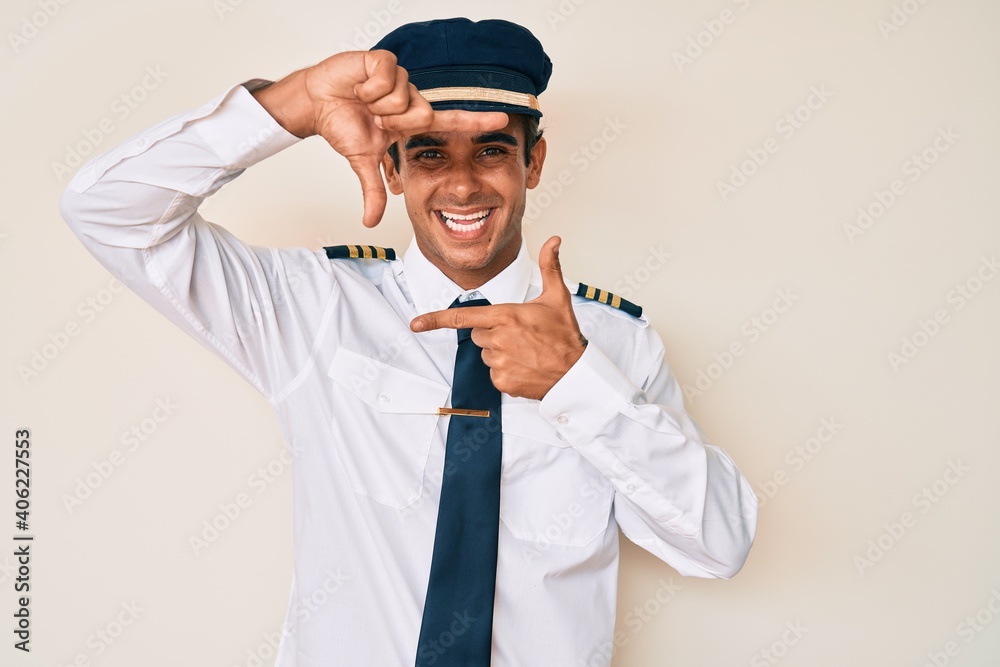 Young hispanic man wearing airplane pilot uniform smiling making frame with hands and fingers with happy face. creativity and photography concept.