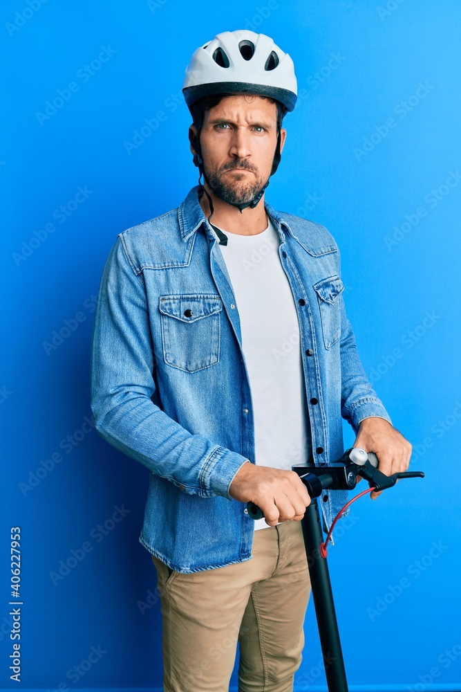 Young handsome man standing on modern scooter wearing helmet skeptic and nervous, frowning upset because of problem. negative person. Young handsome man standing on modern scooter wearing helmet skeptic and nervous, frowning upset because of problem. negative person.