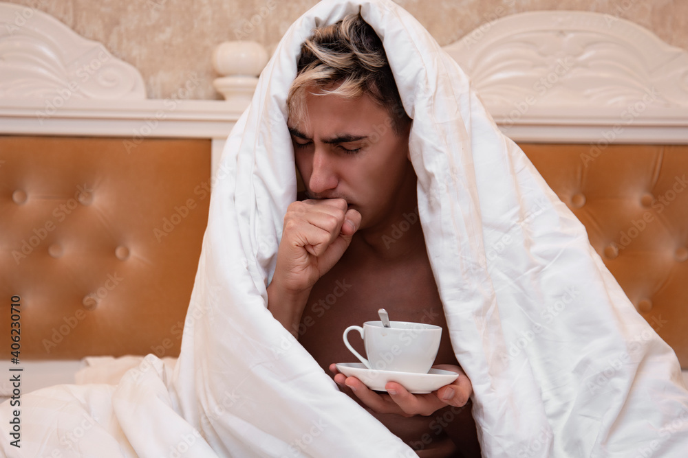 Tired guy sits on the bed over a cup of coffee. Diseases and ailments. Good morning. Tired guy sits on the bed over a cup of coffee. Diseases and ailments. Good morning.