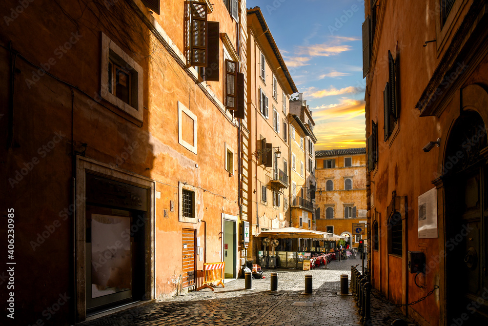 A narrow back alley in the historic center of Rome, Italy, leads to a small sidewalk cafe at sunset.