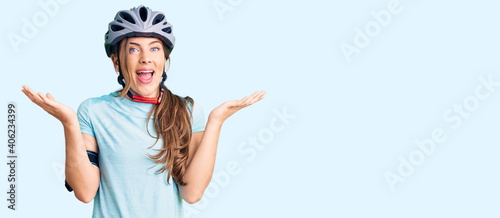 Beautiful caucasian young woman wearing bike helmet celebrating victory with happy smile and winner expression with raised hands