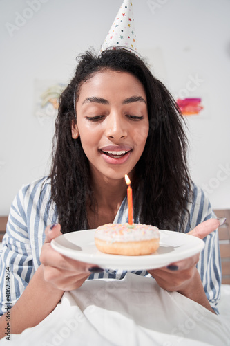 Woman in party cap holding cake and preparing to blowing candle