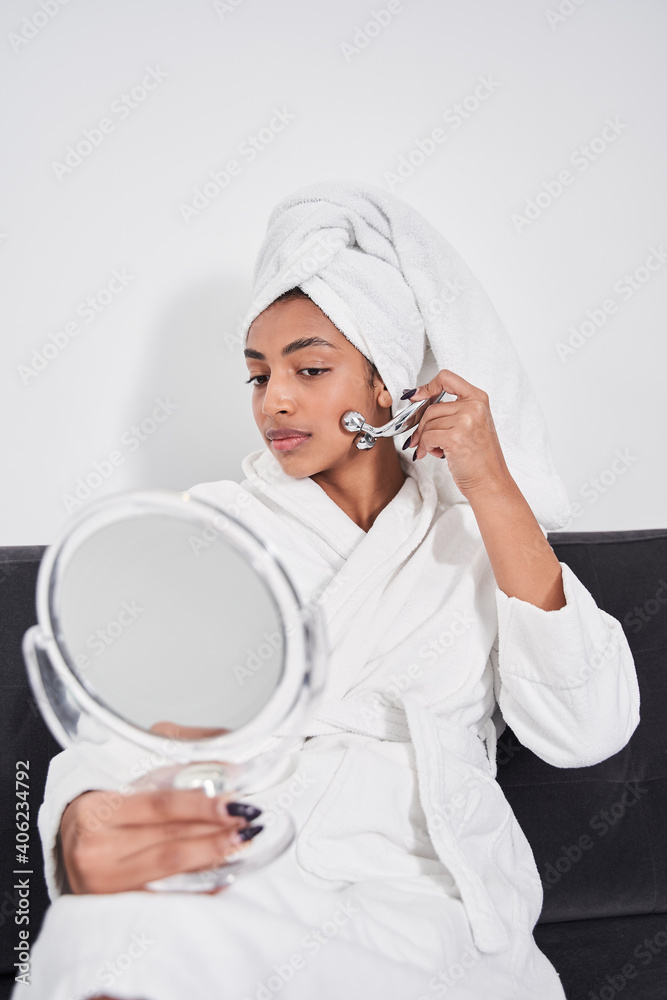 Female wearing bathrobe and doing face massage indoors Female wearing bathrobe and doing face massage indoors