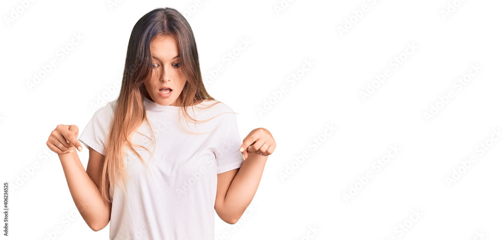 Beautiful caucasian woman wearing casual white tshirt pointing down with fingers showing advertisement, surprised face and open mouth Beautiful caucasian woman wearing casual white tshirt pointing down with fingers showing advertisement, surprised face and open mouth