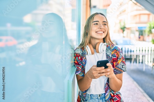 Young beautiful blonde caucasian woman smiling happy outdoors on a sunny day wearing headphones and using smartphone photo