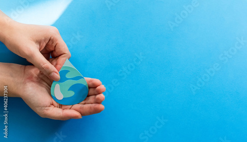 Woman hands holding paper cut water drop on blue background. Clean water and sanitation, saving water. World Water Day. Ecology concept.