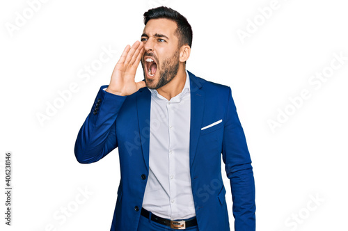 Young hispanic man wearing business jacket shouting and screaming loud to side with hand on mouth. communication concept.