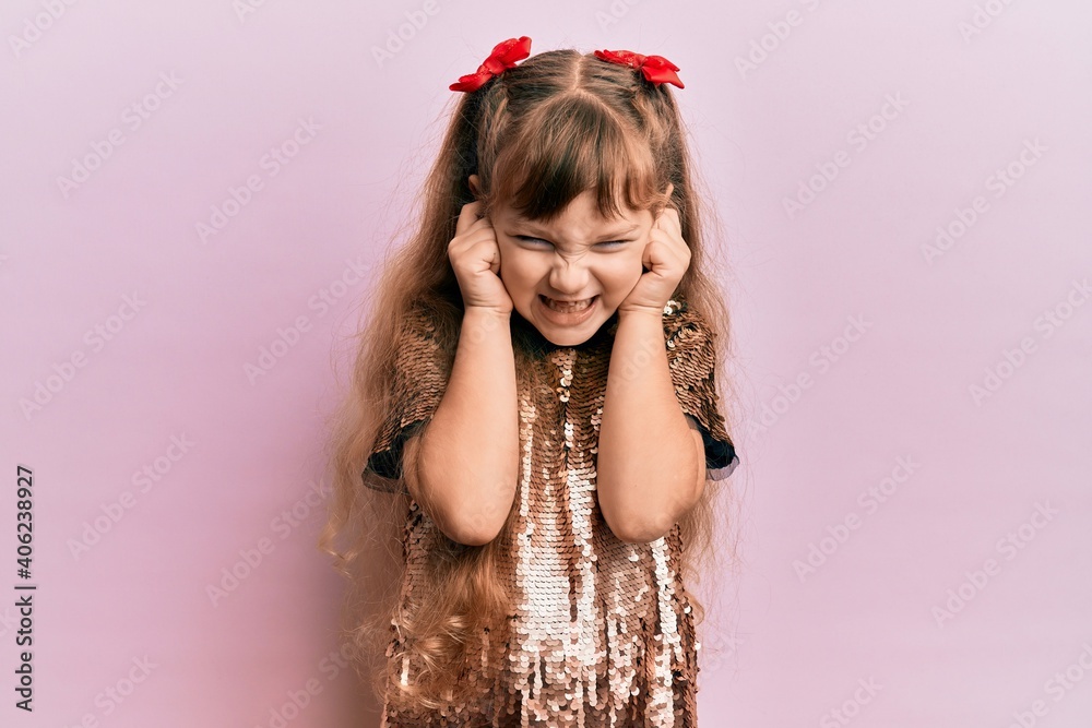 Little caucasian girl kid wearing festive sequins dress covering ears with fingers with annoyed expression for the noise of loud music. deaf concept. Little caucasian girl kid wearing festive sequins dress covering ears with fingers with annoyed expression for the noise of loud music. deaf concept.