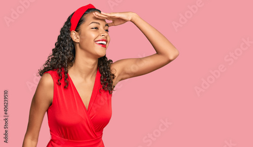 Young african american girl wearing elegant and sexy look very happy and smiling looking far away with hand over head. searching concept.