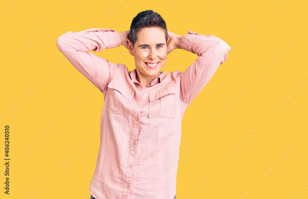 Young woman with short hair wearing casual clothes relaxing and stretching, arms and hands behind head and neck smiling happy Young woman with short hair wearing casual clothes relaxing and stretching, arms and hands behind head and neck smiling happy