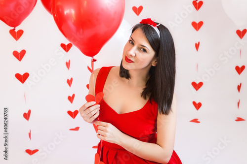 Beautiful girl with red balloons and garland-heart. Portrait of a dark-haired girl with red lipstick. Celebrate Valentine's Day.