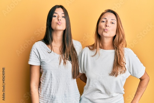 Hispanic family of mother and daughter wearing casual white tshirt looking at the camera blowing a kiss on air being lovely and sexy. love expression.