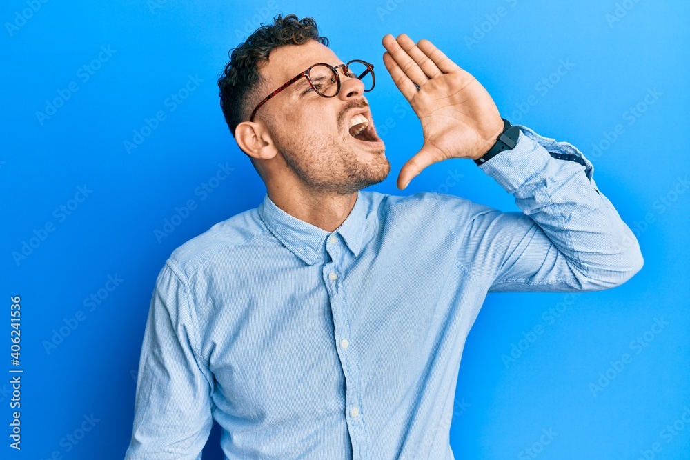 Young hispanic man wearing casual clothes and glasses shouting and screaming loud to side with hand on mouth. communication concept.