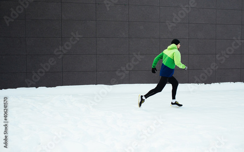 Man athlete running in winter cold and snow. Training during Covid-19 pandemic. Winter exercise to stay fit. Urban city jogger. Smiling man fitness workout. Active and healthy life in quarantine