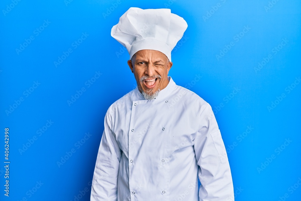 Middle age grey-haired man wearing professional cook uniform and hat winking looking at the camera with sexy expression, cheerful and happy face. Middle age grey-haired man wearing professional cook uniform and hat winking looking at the camera with sexy expression, cheerful and happy face.
