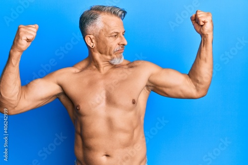 Middle age grey-haired man standing shirtless showing arms muscles smiling proud. fitness concept.