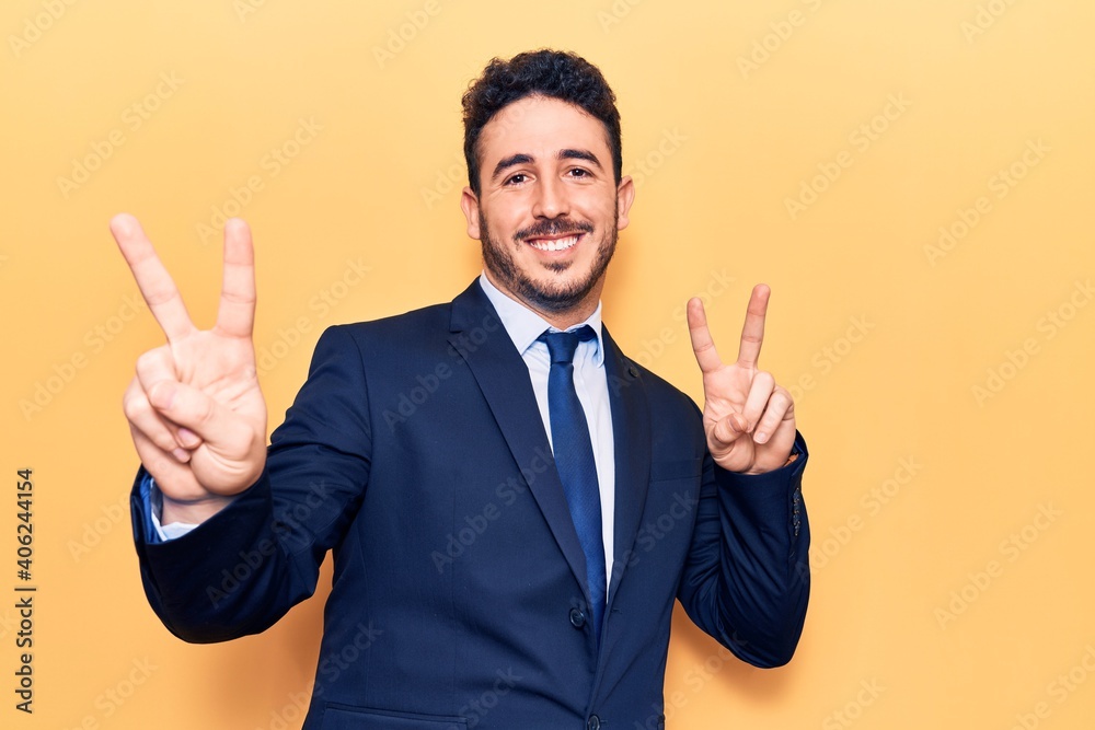 Young hispanic man wearing suit smiling looking to the camera showing fingers doing victory sign. number two. Young hispanic man wearing suit smiling looking to the camera showing fingers doing victory sign. number two.