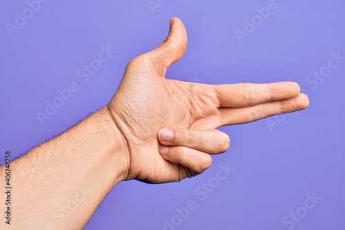 Hand of caucasian young man showing fingers over isolated purple background gesturing fire gun weapon with fingers, aiming shoot symbol