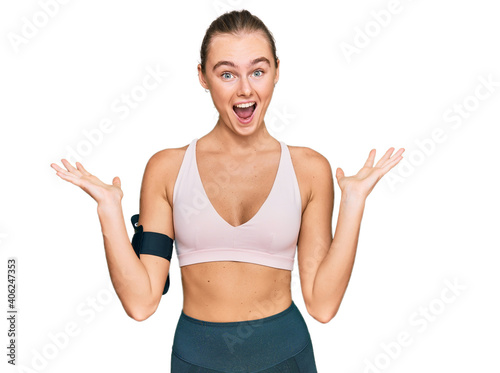 Beautiful young blonde woman wearing sportswear and arm band celebrating victory with happy smile and winner expression with raised hands