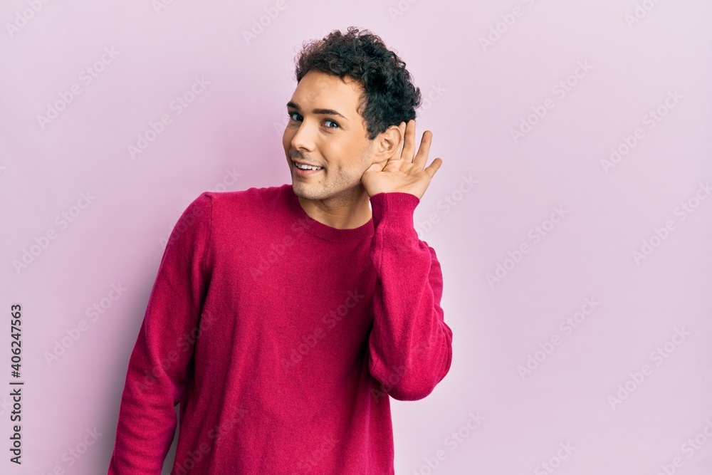 Handsome hispanic man wearing casual clothes over pink background smiling with hand over ear listening and hearing to rumor or gossip. deafness concept. Handsome hispanic man wearing casual clothes over pink background smiling with hand over ear listening and hearing to rumor or gossip. deafness concept.