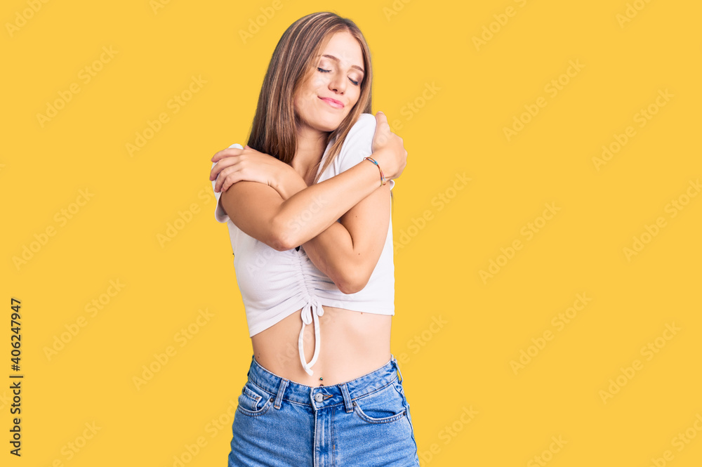 Young beautiful blonde woman wearing casual white tshirt hugging oneself happy and positive, smiling confident. self love and self care Young beautiful blonde woman wearing casual white tshirt hugging oneself happy and positive, smiling confident. self love and self care