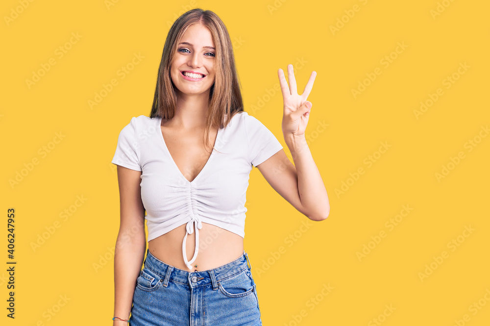 Young beautiful blonde woman wearing casual white tshirt showing and pointing up with fingers number three while smiling confident and happy.