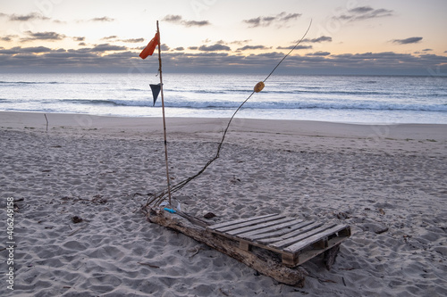 Makeshift wooden raft made from logs and wood planks on a sandy beach with ocean in background.