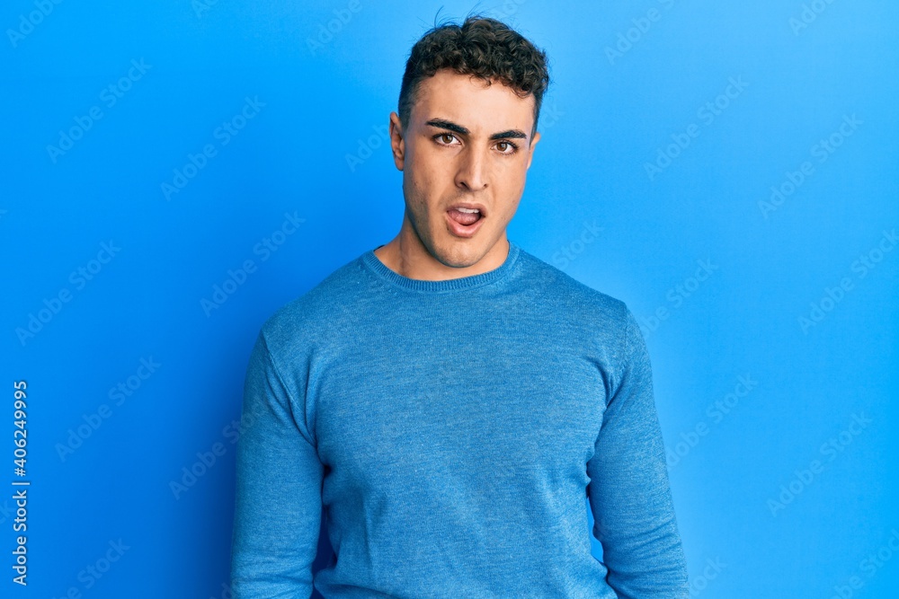Hispanic young man wearing casual winter sweater in shock face, looking skeptical and sarcastic, surprised with open mouth Hispanic young man wearing casual winter sweater in shock face, looking skeptical and sarcastic, surprised with open mouth