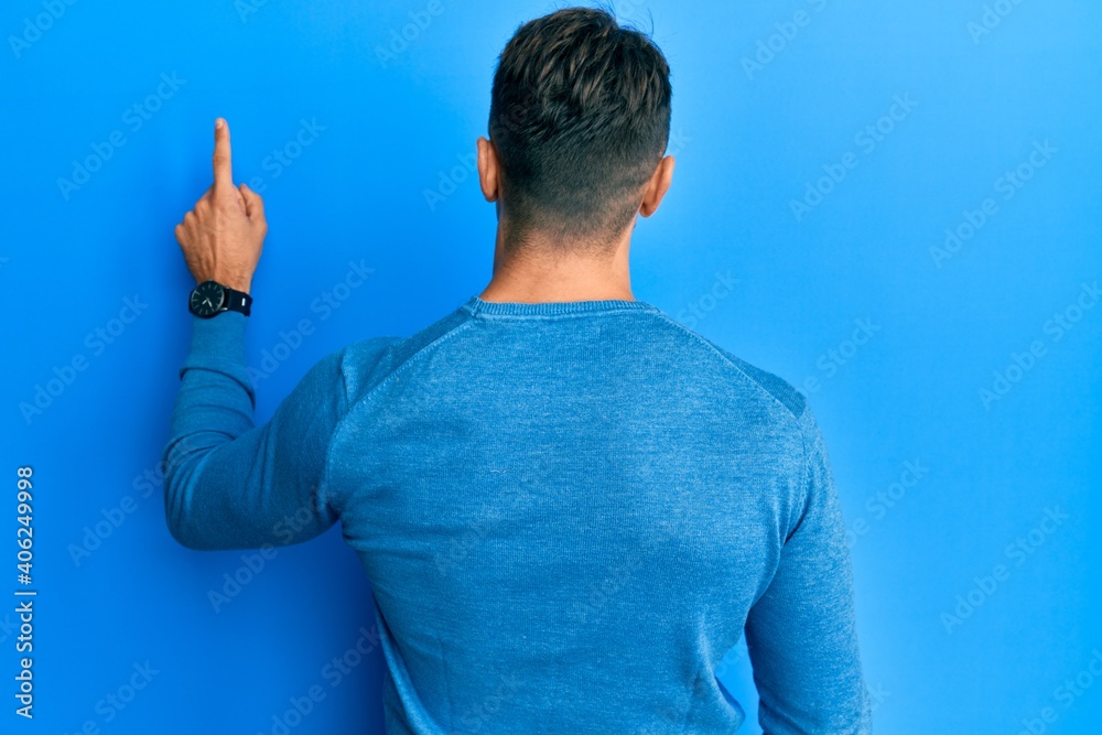Hispanic young man wearing casual winter sweater posing backwards pointing ahead with finger hand Hispanic young man wearing casual winter sweater posing backwards pointing ahead with finger hand