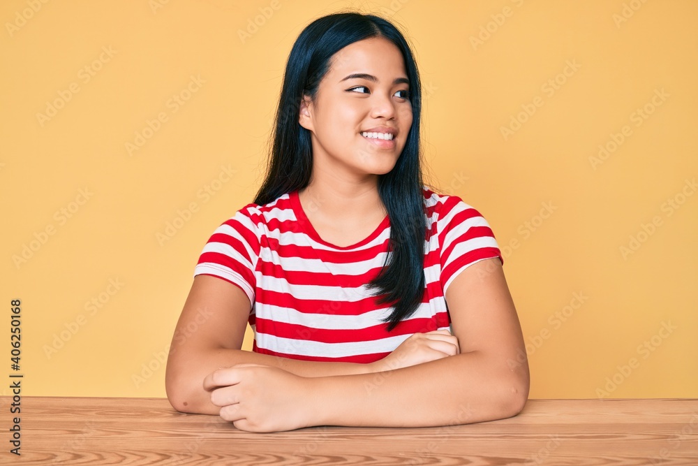 Young beautiful asian girl wearing casual clothes sitting on the table looking to side, relax profile pose with natural face and confident smile. Young beautiful asian girl wearing casual clothes sitting on the table looking to side, relax profile pose with natural face and confident smile.