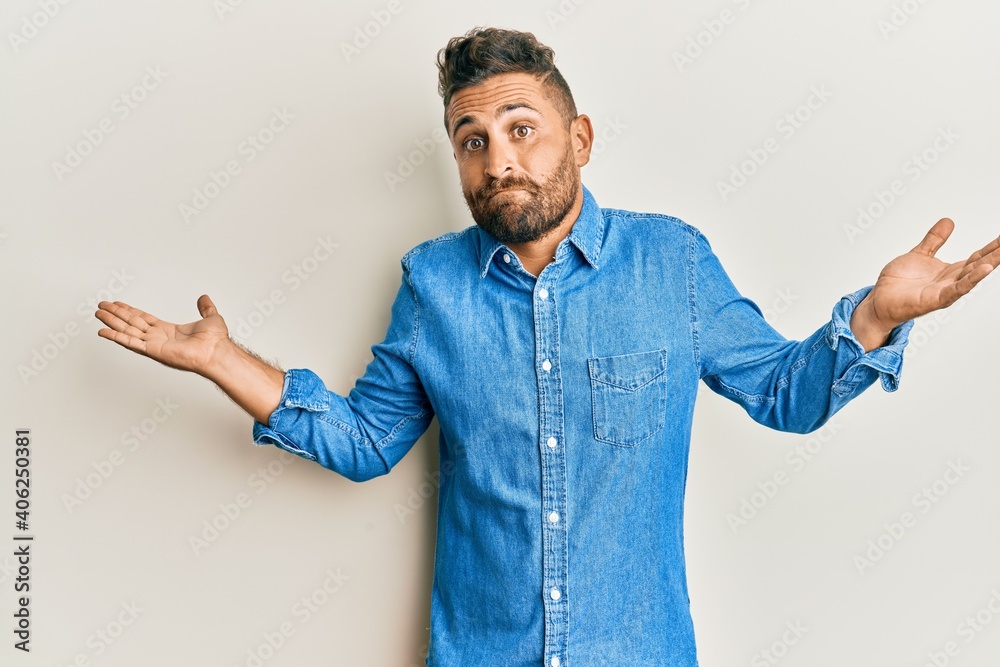 Handsome man with beard wearing casual denim jacket clueless and confused with open arms, no idea and doubtful face. Handsome man with beard wearing casual denim jacket clueless and confused with open arms, no idea and doubtful face.