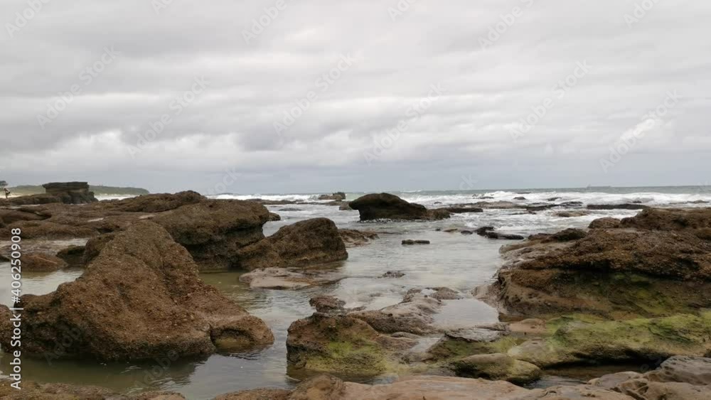 Ocean wave flowing through and around large rocks along the beach front on a cloudy day, Sea Cave, Cave Beach, New South Wales, Australia Ocean wave flowing through and around large rocks along the beach front on a cloudy day, Sea Cave, Cave Beach, New South Wales, Australia