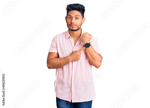 Handsome latin american young man wearing casual summer shirt in hurry pointing to watch time, impatience, looking at the camera with relaxed expression