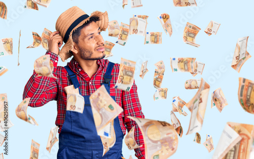 Handsome latin american young man weaing handyman uniform confuse and wondering about question. uncertain with doubt, thinking with hand on head. pensive concept.