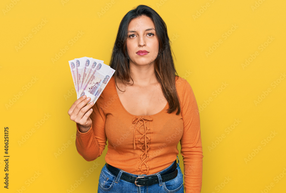Beautiful hispanic woman holding russian 500 ruble banknotes thinking attitude and sober expression looking self confident Beautiful hispanic woman holding russian 500 ruble banknotes thinking attitude and sober expression looking self confident