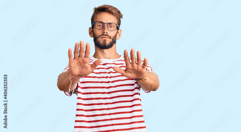 Naklejka premium Handsome blond man with beard wearing casual clothes and glasses doing stop gesture with hands palms, angry and frustration expression